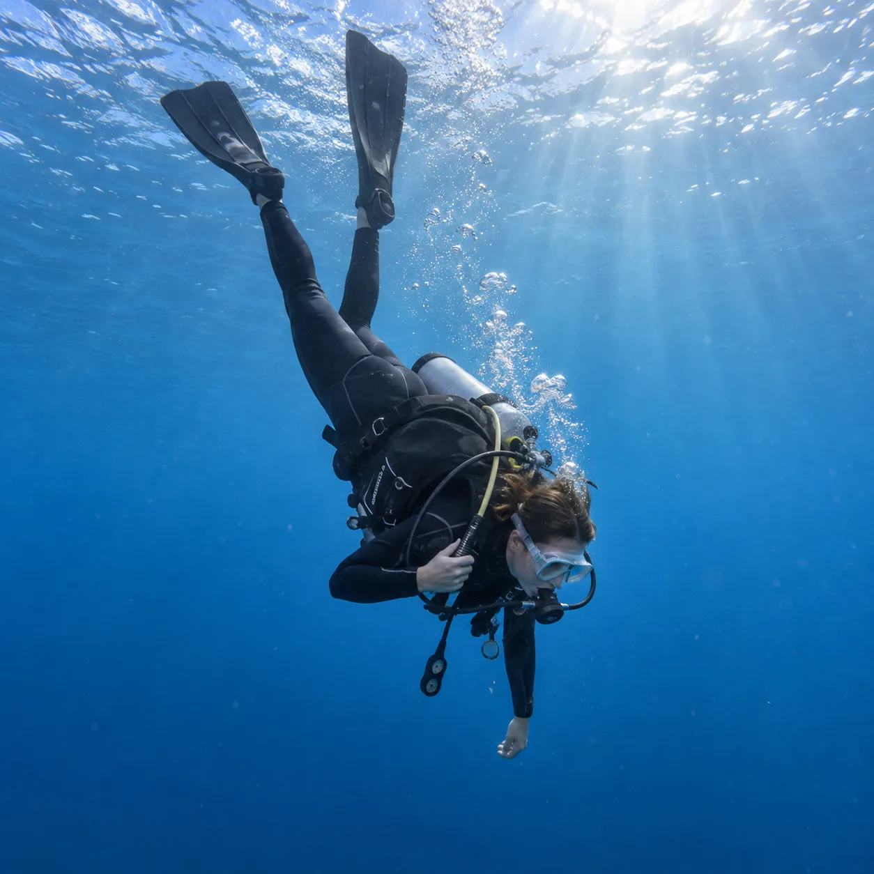 A diver with a scuba tank, regulator and BCD swims head down and feet up, illustrating difficulty descending with too little weight.